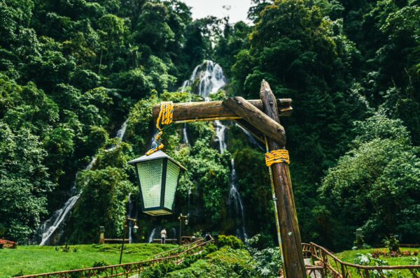 Relaxing green landscape with a rustic lantern in the foreground and waterfalls cascading through lush trees in Termales Rosa, Risaralda, Colombia.