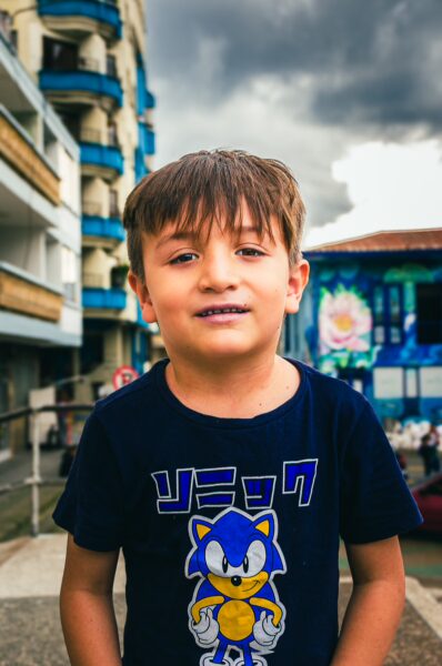 A smiling boy wearing a Sonic the Hedgehog shirt stands in front of colorful buildings in Santa Rosa de Cabal, Risaralda, Colombia.