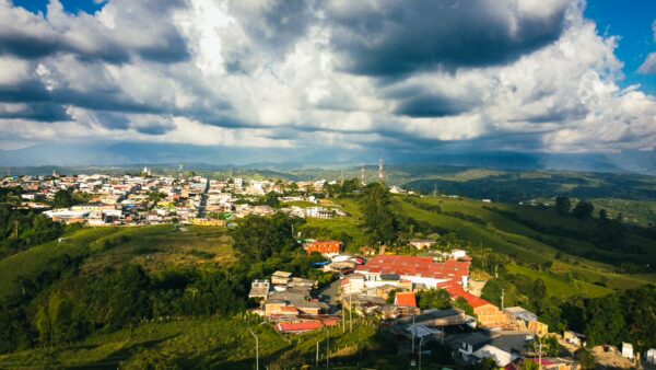 Colorful rooftops blend with lush green hills under a dramatic sky, showcasing the scenic beauty of Filandia, Quindío, Colombia.