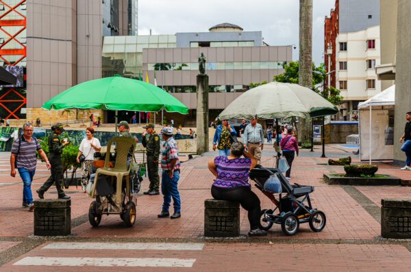 Vibrant scene in Plaza de Bolívar, Armenia, Quindío, Colombia, featuring market stalls, umbrellas, and people enjoying the outdoors.