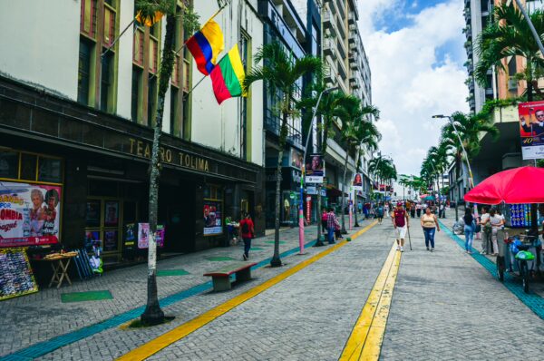 Vibrant street scene in Ibagué, Colombia, featuring palm trees, colorful flags, and shops along a pedestrian walkway.