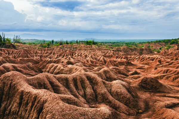 Rust-colored labyrinth of eroded terrain with sparse green vegetation under a cloudy sky in Tatacoa Desert, Huila, Colombia.