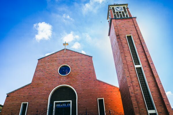 Red brick church with a tall clock tower against a blue sky in Montenegro, Quindio, Colombia.