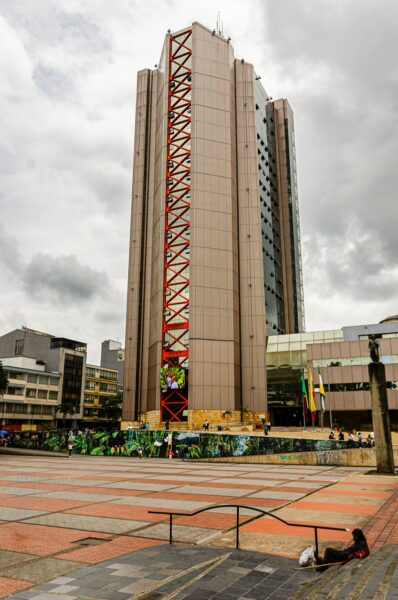 Modern architecture contrasts against the cloudy sky at Plaza de Bolívar, Armenia, Quindio, Colombia, with vibrant street art nearby.