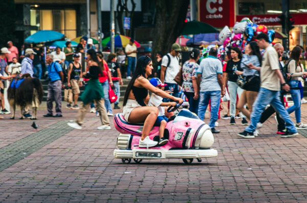 Colorful bustling scene at Plaza de Bolívar in Pereira, Risaralda, with a woman riding a toy car among lively crowds.