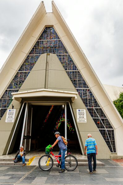 Cathedral of Immaculada Concepción features a striking triangular design, with visitors and cyclists enjoying the area in Armenia, Quindío, Colombia.