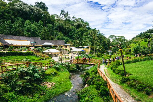Colorful hot springs surrounded by lush greenery, walking paths, and visitors enjoying the natural beauty at Termales Rosa, Risaralda, Colombia.