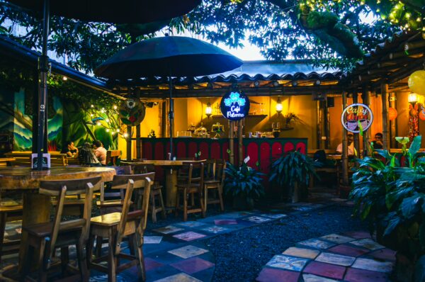 Vibrant café in Arakataka, Pereira, Colombia, featuring colorful stone pathways, wooden tables, and lush tropical plants.