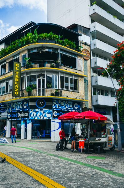 Colorful street scene in Ibagué, featuring a vibrant building with plants, a food cart, and urban activity.