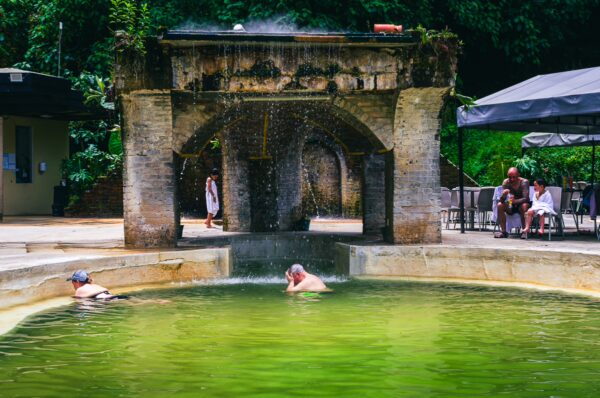 Relaxing guests soak in the green waters of Termales Rosa, framed by rustic stone architecture in Risaralda, Colombia.