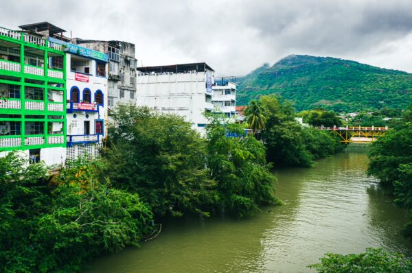 Colorful buildings line the green banks of the river in Honda, Tolima, with lush mountains rising in the background.