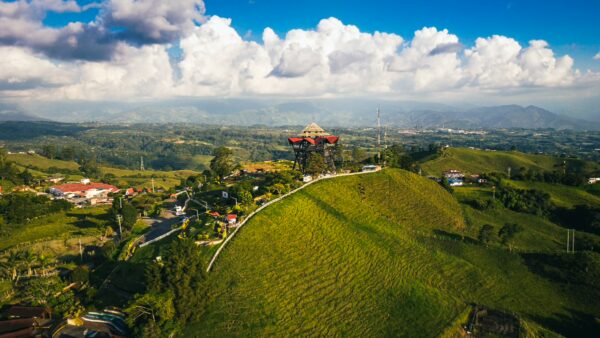 Vibrant green hills surround the Mirador Colina Iluminada in Filandia, Quindío, Colombia, under a bright blue sky with fluffy clouds.