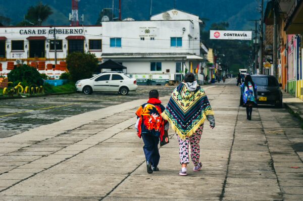 Two people stroll along a cobblestone street in Murillo, Tolima, Colombia, dressed in vibrant traditional clothing.