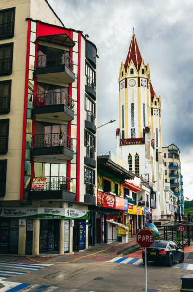 Colorful buildings line the street, featuring a prominent clock tower and a mix of shops in Santa Rosa de Cabal, Risaralda, Colombia.