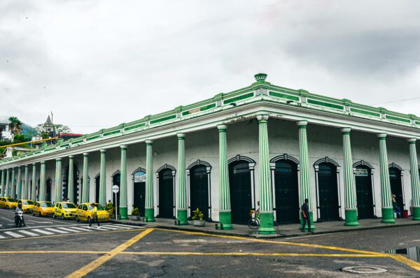 Vibrant green columns support the historic Plaza de Mercado in Honda, Tolima, with yellow taxis parked nearby.