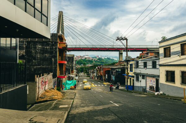 Viaducto de Pereira arches over a vibrant street in Risaralda, Colombia, with yellow taxis and colorful buildings lining the road.
