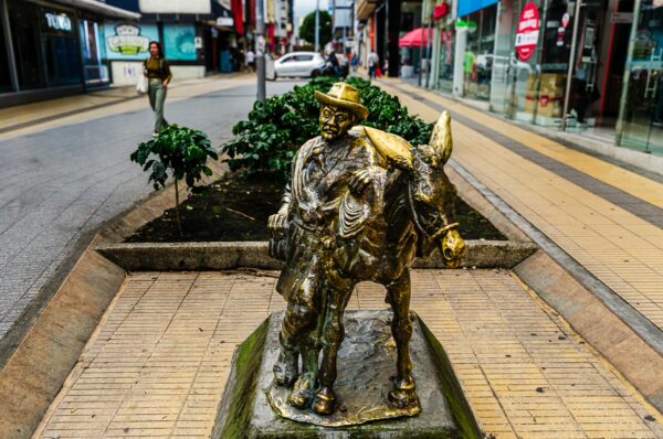 Bronze statue of a man with a horse on Carrera 14, showcasing the vibrant streets of Armenia, Quindío, Colombia.