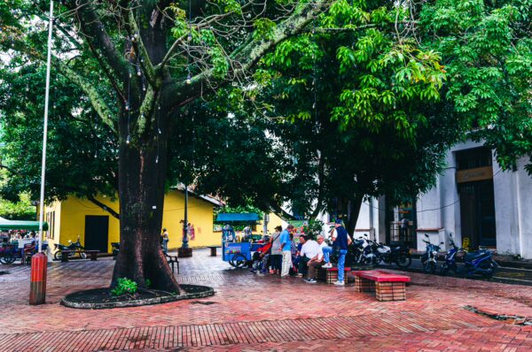Vibrant scene in Honda, Tolima, Colombia, featuring locals gathered under lush trees in a lively plaza.