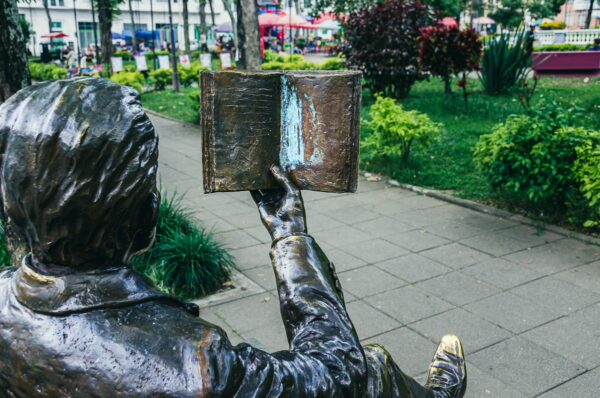 Bronze statue reading a book, surrounded by greenery in Plaza de Bolívar, Ibagué, Tolima, Colombia. Vibrant atmosphere.