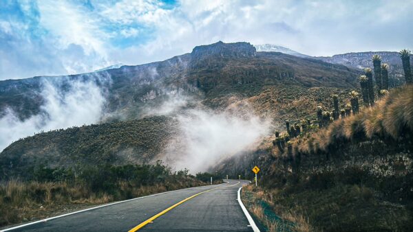 Winding road curves through misty mountains near Nevado del Ruiz, showcasing green hills and dramatic clouds in Tolima, Colombia.