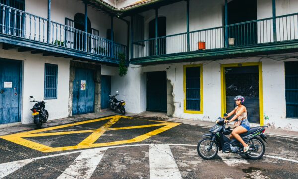 A motorcyclist rides through a colorful courtyard in Tolima, Colombia, surrounded by vibrant blue and yellow buildings.