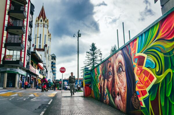 Vibrant mural depicting an indigenous face along the street, with modern buildings and a tower in Santa Rosa de Cabal, Risaralda.