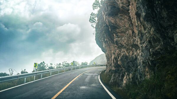 Winding road alongside a rocky cliff under a cloudy sky, capturing the serene landscape of Nevado del Ruiz, Tolima, Colombia.
