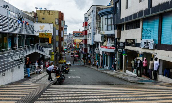 Colorful shops line a steep street in Armenia, Quindío, Colombia, with bustling activity and a vibrant atmosphere.