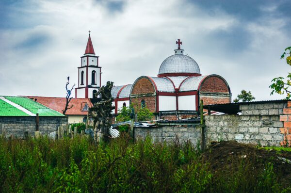 Colorful Murillo church juxtaposed with green fields and overcast skies, showcasing the charm of Medellia, Tolima, Colombia.