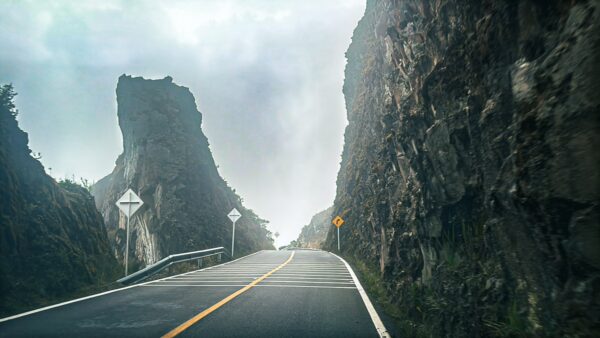 Winding road flanked by steep rock formations in a misty landscape near Nevado del Ruiz, Tolima, Colombia.