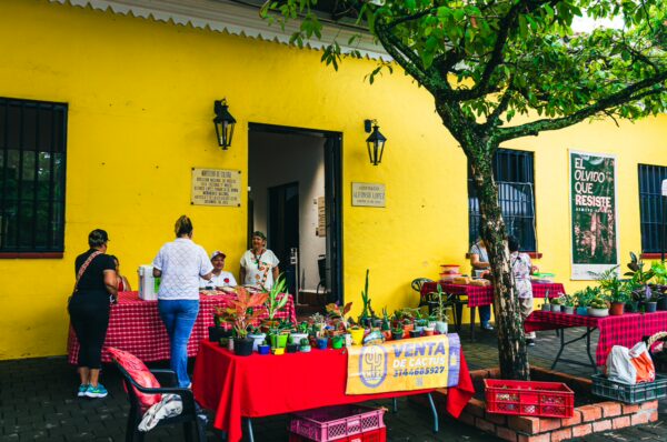 Casa Alfonso López Pumarejo features vibrant yellow walls, with tables displaying potted plants and locals engaging in conversation.