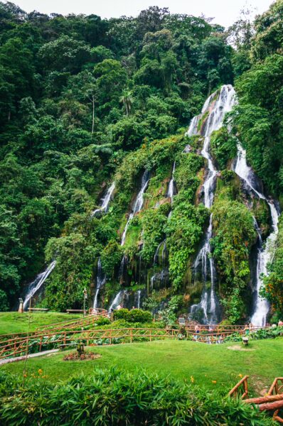 Lush green landscape with cascading waterfalls at Termales del Ruiz in Risaralda, Colombia, surrounded by vibrant foliage.