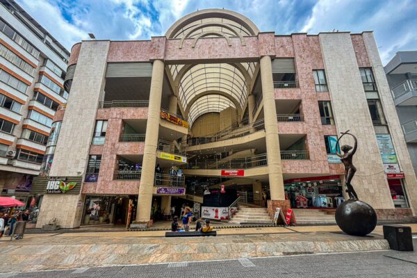 Carrera 14 features vibrant shops and a striking modern building design in Armenia, Quindío, Colombia, under a dramatic sky.
