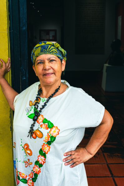 Traditional attire and warm smile of a woman with colorful headscarf, captured in a vibrant setting in Tolima, Colombia.