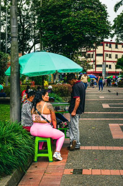 Colorful scene at Parque La Libertad in Pereira, Risaralda, with visitors relaxing under umbrellas along the walkway.