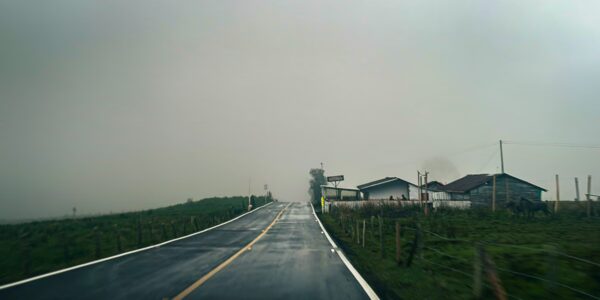 Lush green fields line the wet road leading to rustic houses in the misty landscape near Nevado del Ruiz, Tolima, Colombia.
