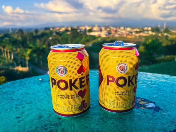 Brightly colored Poker beer cans sit on a table, with a scenic view of Filandia, Quindio, Colombia, in the background.