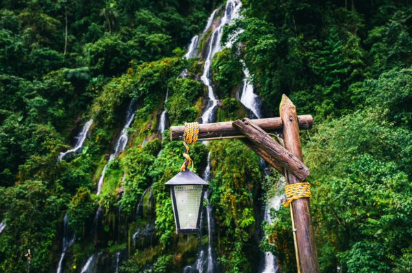 Lush green foliage surrounds a wooden lantern post near cascading waterfalls at Termales Rosa in Risaralda, Colombia.