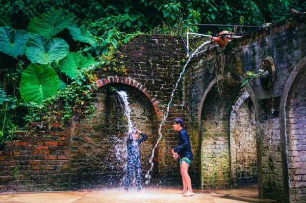Natural springs with water cascading from stone arches into a lush green setting, featuring two children playing in Risaralda, Colombia.