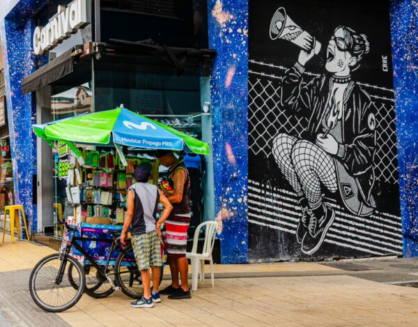 Street vendors near a vibrant mural in Armenia, Quindío, showcase local goods under a bright green canopy.
