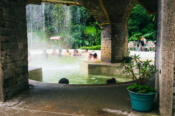 Relaxing visitors enjoy thermal waters beneath a stone archway at Termales Rosa in Risaralda, Colombia, surrounded by lush greenery.