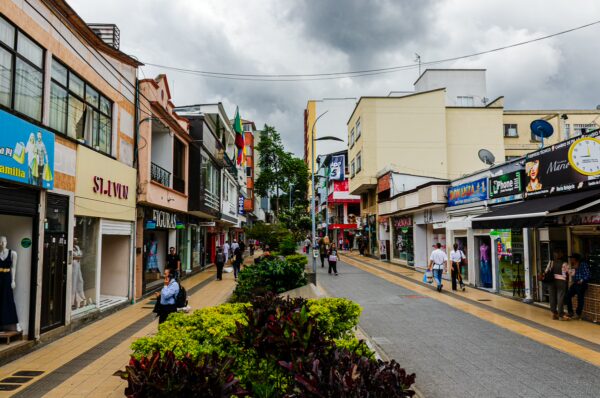 Bustling Carrera 14 in Armenia, Quindío, Colombia, showcases colorful shops, lively pedestrians, and overcast skies.