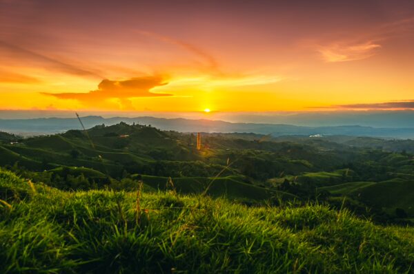 Vibrant sunset over rolling green hills at Mirador Colina Iluminada, Filandia, Quindío, Colombia, capturing warm golden tones.