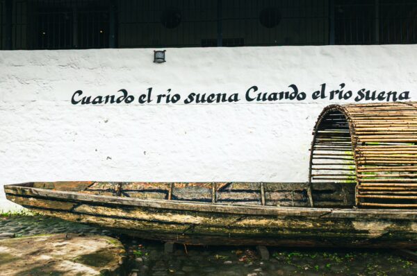 Rustic wooden boat displayed against a white wall, featuring the text "Cuando el río suena" at Museo del Río Magdalena, Honda, Tolima.