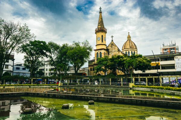 Historic church with a tall spire overlooks the green waters of Parque El Lago in Pereira, Risaralda, Colombia.