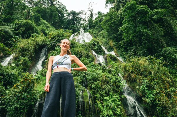 Flowing waterfalls cascade through lush greenery at Termales de Rosa in Risaralda, Colombia, with a visitor posing in the foreground.