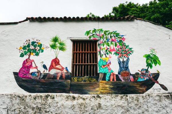 Colorful mural depicting people in a boat adorned with plants, showcasing vibrant art in Honda, Tolima, Colombia.