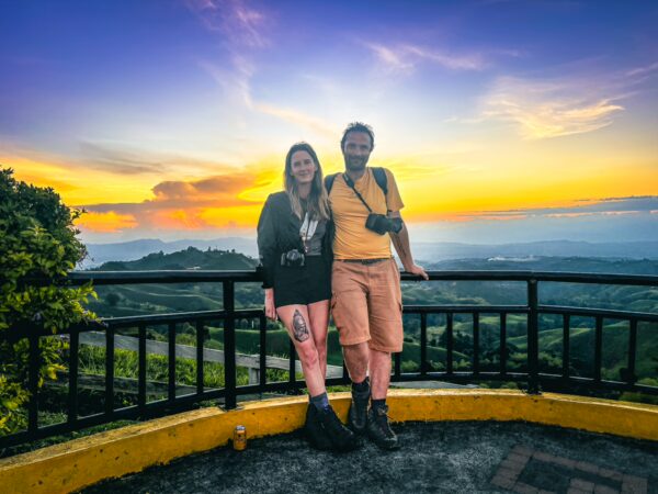 Couple poses at the Mirador Colina Iluminada, enjoying a vibrant sunset over the lush hills of Filandia, Quindio, Colombia.