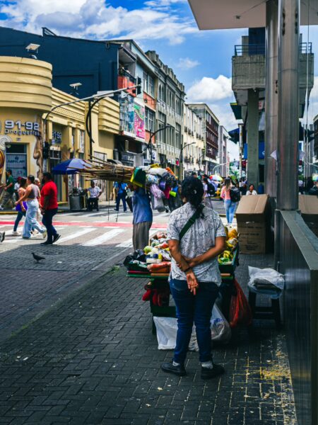 Colorful street market in Pereira, Risaralda, Colombia, with vendors, shoppers, and vibrant displays under a bright blue sky.