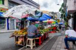 Vibrant street scene in Quindio, Colombia, featuring colorful market stalls selling fresh fruits under canopies.